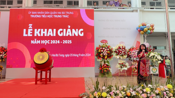 Cô giáo mầm non đang dắt tay học sinh nhỏ trên sân trường, tượng trưng cho những bước đi đầu tiên